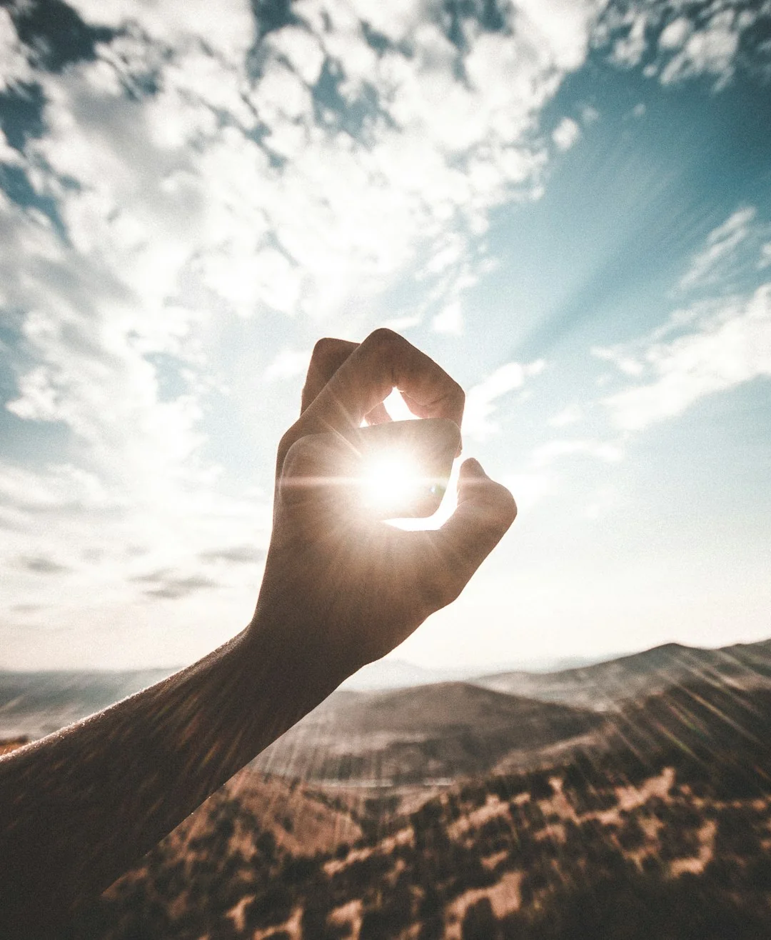Mão a segurar a luz do sol contra um céu de montanha